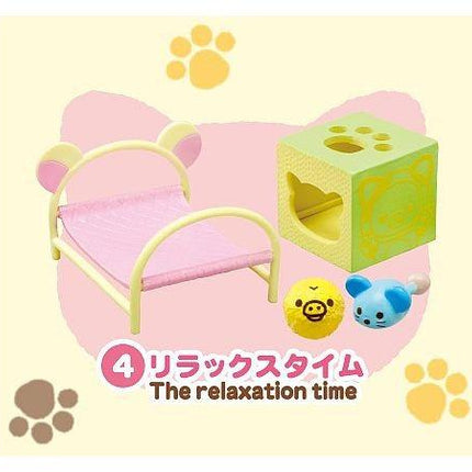 A pink bed with a yellow cat head on it, along with a green cube-shaped toy and a yellow ball, all set against a yellow background with paw prints.