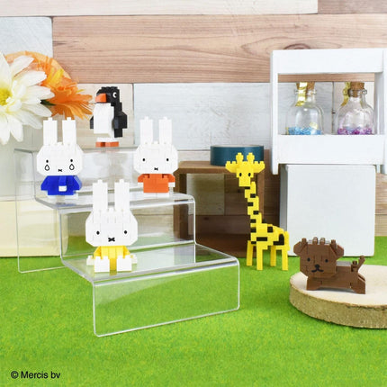 A collection of colorful, small toy figurines, including a penguin, rabbit, giraffe, and dog, arranged on a green surface.