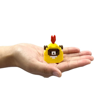 A hand holding a small yellow and red toy with a face on it.