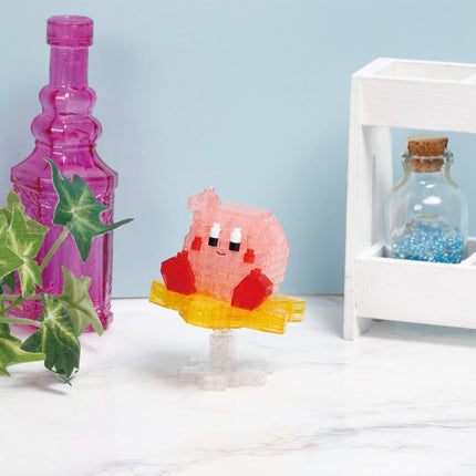 a pink, cartoon-like character sitting on a yellow base, surrounded by various objects such as a pink bottle, a white wooden crate, and a glass bottle with blue beads.