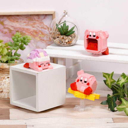 a collection of three small, colorful toys, including a pink and purple character, a pink and red character, and a pink and yellow character, all sitting on a white surface. The toys are surrounded by various decorative elements, such as a potted plant, a glass vase, and a framed picture.
