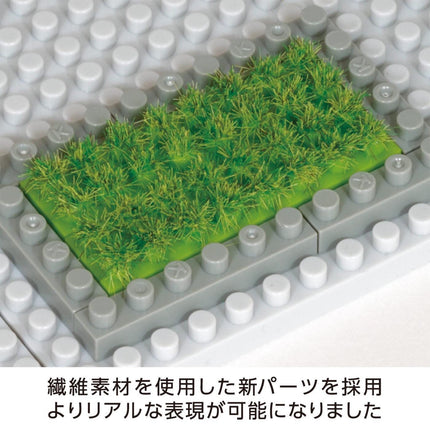 A close-up image of a green grass-like material placed on a white surface, surrounded by gray and white Lego bricks.