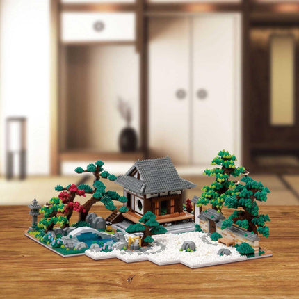 A miniature Japanese-style garden with a small wooden house, trees, and a pond, all crafted from building blocks.
