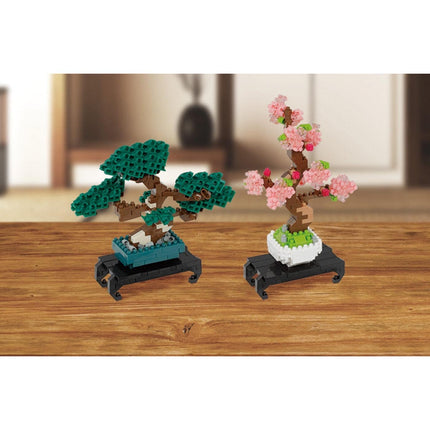 Two small bonsai trees made of colorful building blocks, one with green leaves and the other with pink flowers, placed on a wooden surface.