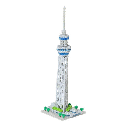 A white and blue Lego tower with a pointed spire, standing on a base with green trees.