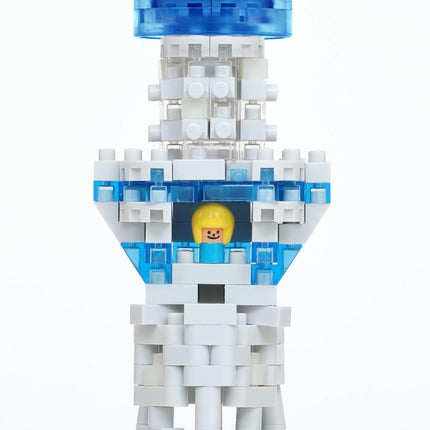 A close-up of a white and blue Lego structure with a yellow figure inside, set against a white background.