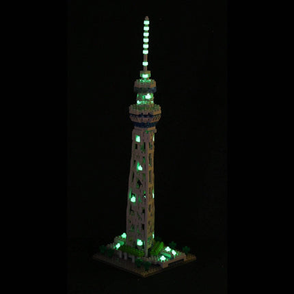 A tall, illuminated tower made of small, glowing blocks stands against a dark background.