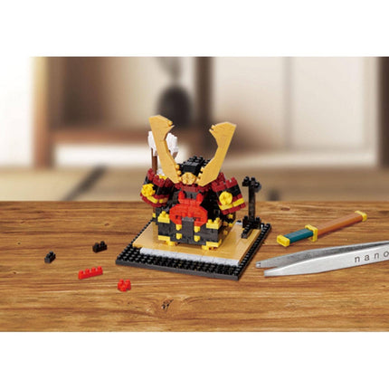 A small, colorful toy resembling a warrior or knight figure is sitting on a wooden surface, surrounded by various building block pieces.