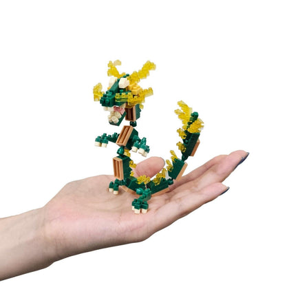 A hand holding a small green and yellow dragon-shaped toy made of small building blocks.