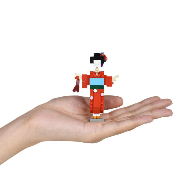 A hand holding a small, colorful toy figure of a geisha against a white background.