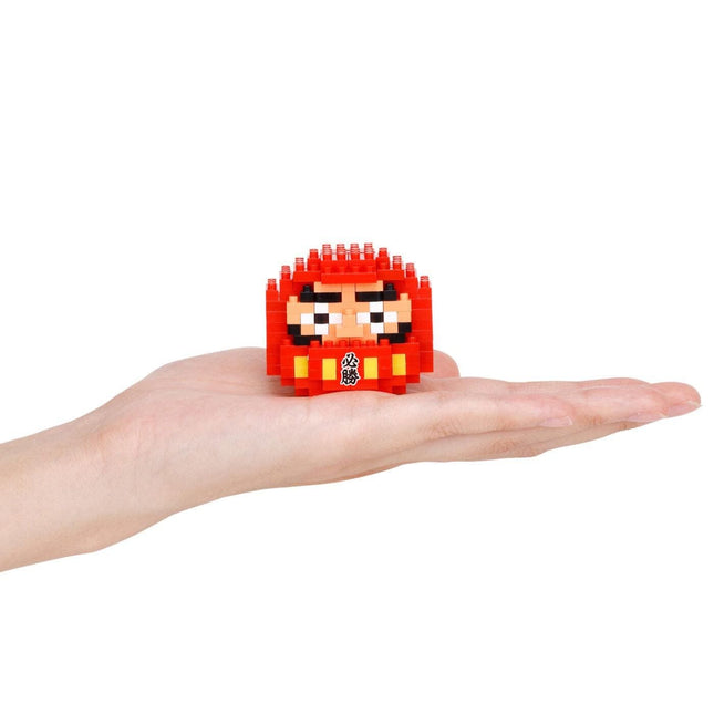 A hand holding a small red, pixelated character resembling a doll or dollhouse.