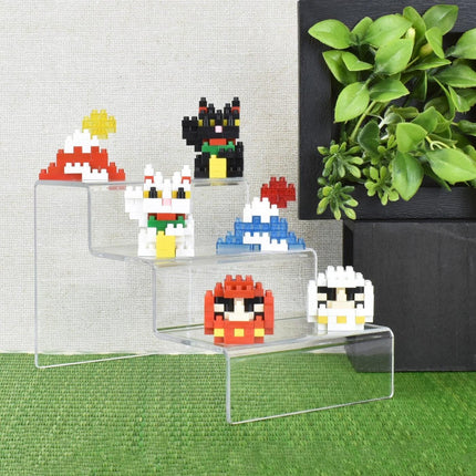 A display of colorful, pixelated character figurines on a clear, three-tiered stand, with a potted plant in the background.
