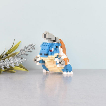 A small, colorful, pixelated figurine of a character from a video game is sitting on a reflective surface, surrounded by a few small white flowers.