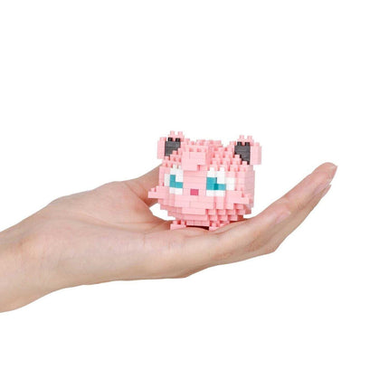 A hand holding a small pink, pixelated character with blue eyes.