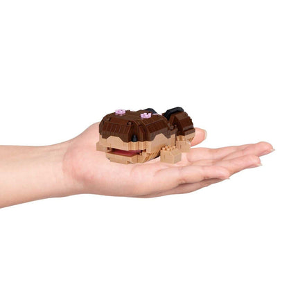 A person's hand holding a small, brown and beige toy fish.