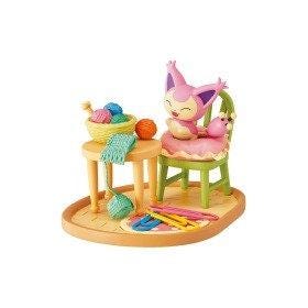 A figurine depicting a pink cat sitting on a green chair, surrounded by various objects such as a bowl of yarn, a green table, and a pink stuffed animal.