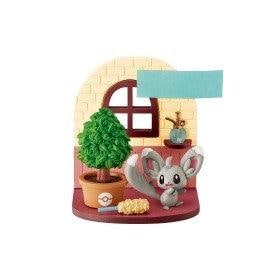 A small figurine of a gray cat with large ears, sitting on a red platform next to a potted plant and a toy tree.