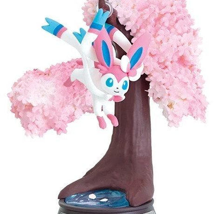 A figurine of a pink and white Pokémon character, resembling Pokémon, is displayed on a tree-like base with pink flowers.