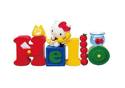 A Hello Kitty figurine is sitting on top of a blue block, surrounded by various colorful toys such as a yellow telephone, a red apple, a blue fishbowl, and a green toy car.