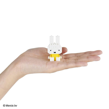 A hand holding a small white and yellow toy rabbit.