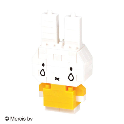 A small, white, and yellow toy rabbit with two black tear drop eyes and a yellow shirt.