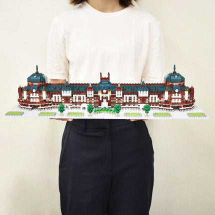 A person is holding a large, intricate model of a building made out of small, colorful bricks.