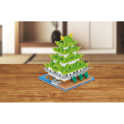 A colorful, multi-layered building made of small, green and white building blocks, resembling a castle or palace, sitting on a wooden surface.