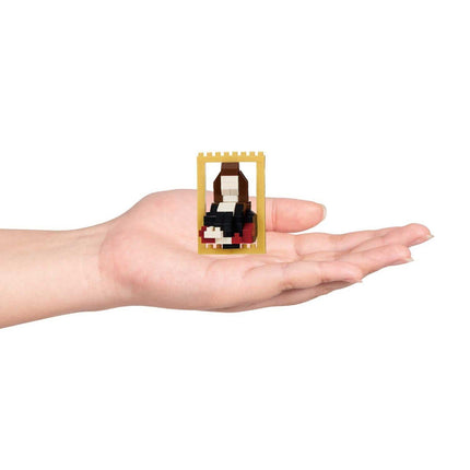 A hand holding a small, yellow-framed object containing a small, black and red figure.