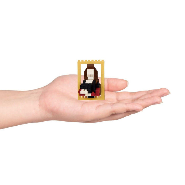 A hand holding a small, yellow-framed object containing a small, black and red figure.