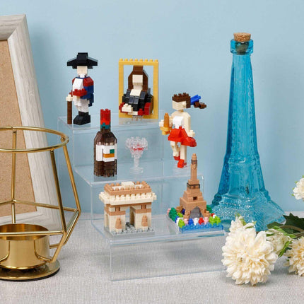 a collection of miniature figurines and objects, including a blue bottle, a golden candlestick holder, and a framed picture, all displayed on a shelf or table.