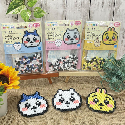 three packages of bead characters, each with a different color and design, arranged on a wooden stand. There are also three pixel art bead characters in the foreground, and a potted plant and a sunflower can be seen in the background.