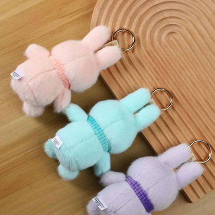 Three small, plush rabbits in different pastel colors - pink, light blue, and purple - are arranged on a wooden surface.