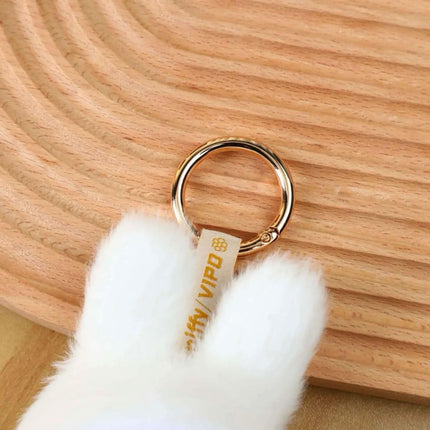 A close-up view of a white furry object, possibly a plush toy or stuffed animal, attached to a gold ring.