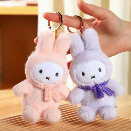 A hand holding two plush toy rabbits, one pink and one purple, with metal rings attached to them.