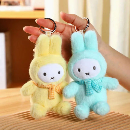 A person's hand holding two plush bunny keychains, one in a yellow color and the other in a light blue color.