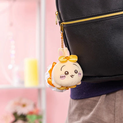 White plush mini mascot keychain with yellow bow, attached to a black bag.