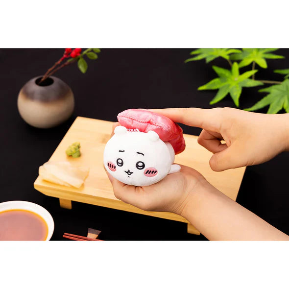 Sushi mascot plush toy with white face and red topping, held near chopsticks