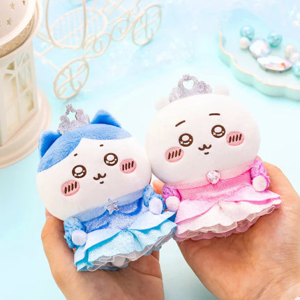 White plush mascots with blue and pink ruffled outfits and bead crowns, held in hands.