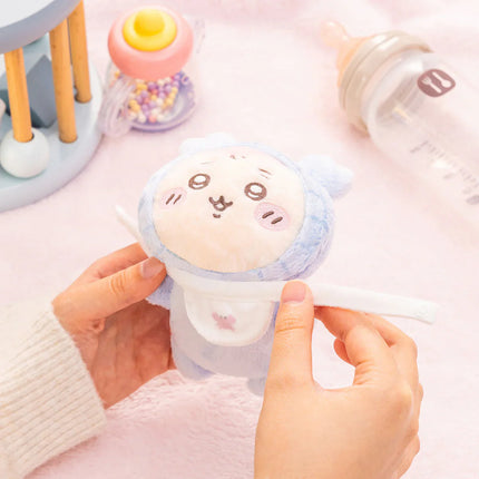 Light-blue crawling plush toy with embroidered face and small tail, held by hands